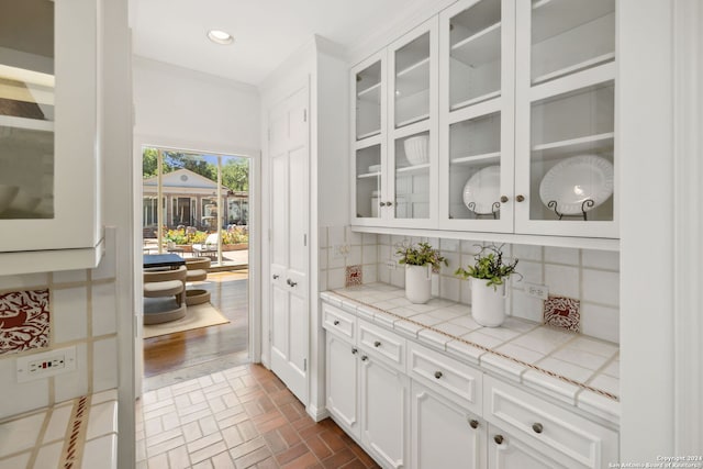 bar with ornamental molding, tile countertops, white cabinets, and backsplash