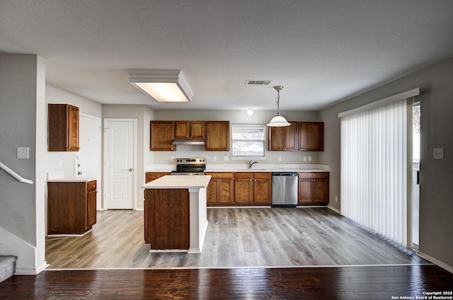 kitchen featuring sink, stainless steel appliances, a textured ceiling, decorative light fixtures, and light wood-type flooring