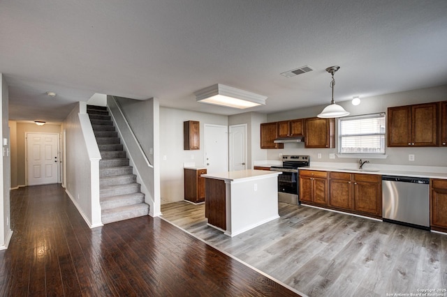 kitchen with sink, stainless steel appliances, a kitchen island, decorative light fixtures, and light wood-type flooring