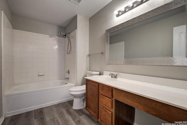 full bathroom featuring hardwood / wood-style floors, tiled shower / bath combo, vanity, toilet, and a textured ceiling