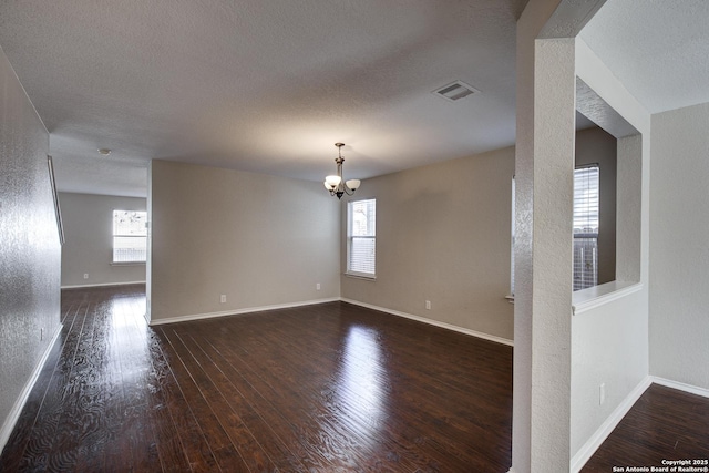 empty room featuring dark wood-type flooring, a textured ceiling, and a chandelier