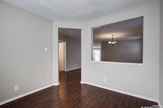 spare room with dark hardwood / wood-style flooring, a textured ceiling, and a notable chandelier