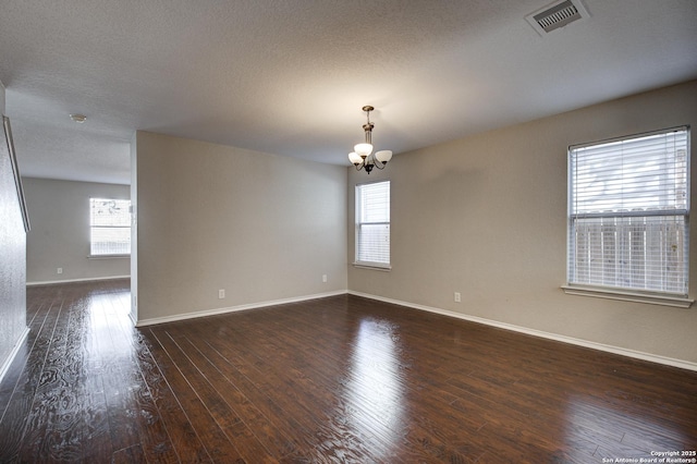 unfurnished room featuring a notable chandelier, a textured ceiling, dark hardwood / wood-style floors, and a healthy amount of sunlight