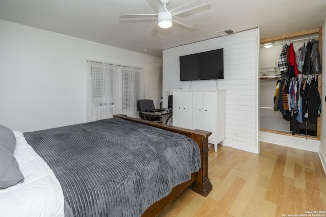 bedroom with a walk in closet, light hardwood / wood-style floors, a closet, and ceiling fan