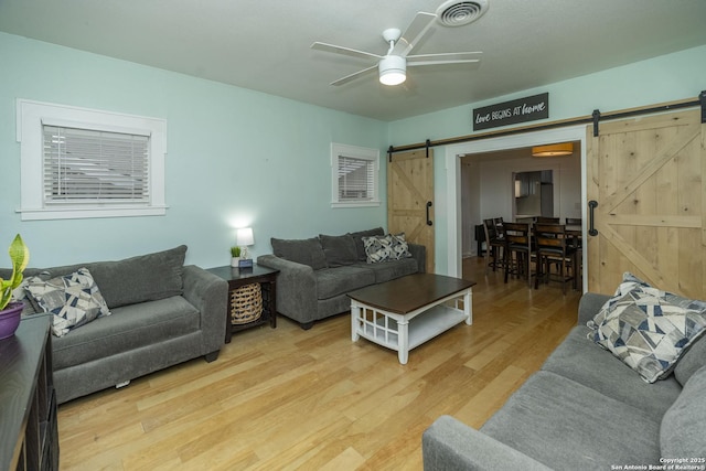 living room featuring ceiling fan, wood-type flooring, and a barn door