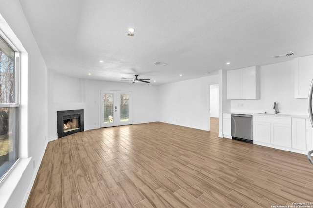 unfurnished living room featuring ceiling fan, sink, light hardwood / wood-style flooring, and a textured ceiling