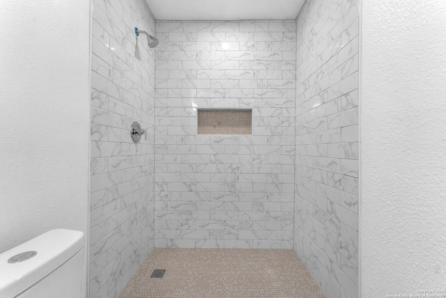 bathroom with a tile shower and toilet