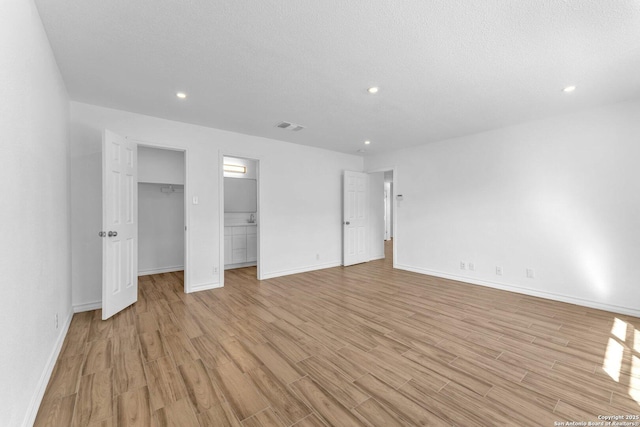 unfurnished bedroom featuring a spacious closet, light hardwood / wood-style floors, and a textured ceiling