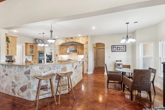 kitchen with a chandelier, light brown cabinets, double oven, dark tile patterned floors, and pendant lighting