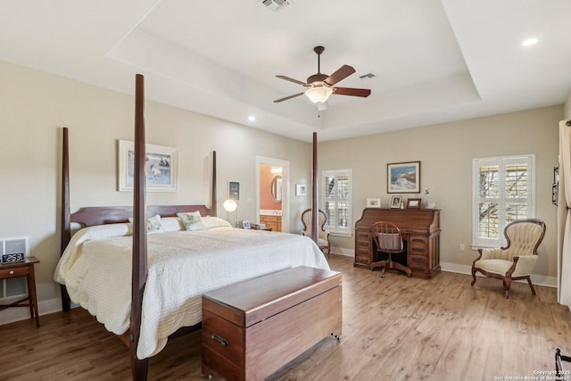 bedroom featuring connected bathroom, a tray ceiling, light hardwood / wood-style flooring, and ceiling fan