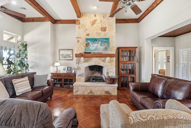 tiled living room with ceiling fan, a stone fireplace, a healthy amount of sunlight, and beam ceiling