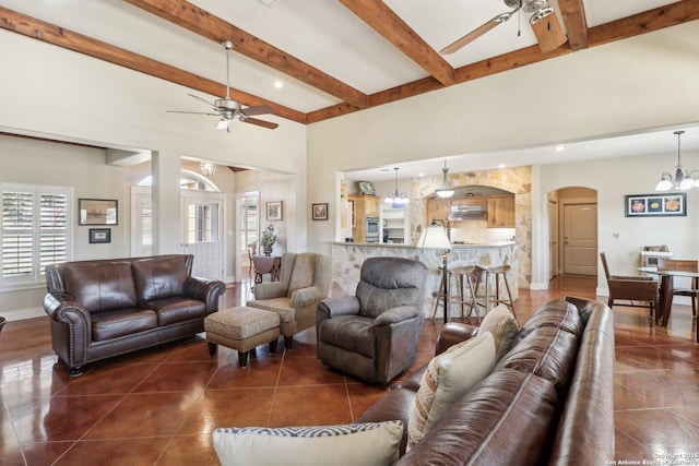 living room featuring ceiling fan with notable chandelier, dark tile patterned flooring, and beam ceiling