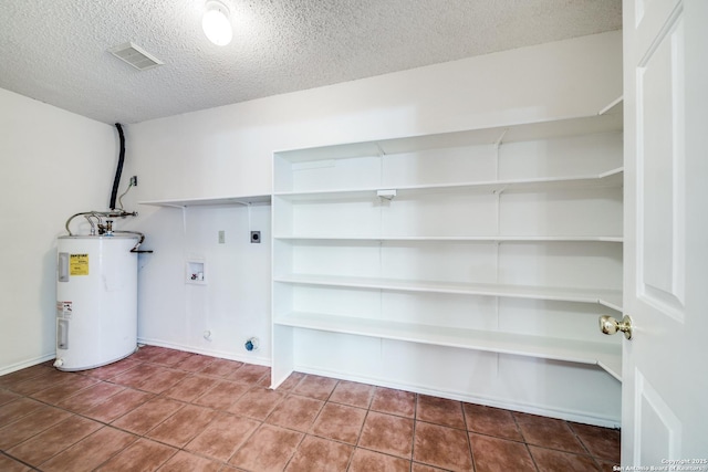 laundry room featuring a textured ceiling, hookup for a washing machine, electric water heater, hookup for an electric dryer, and tile patterned flooring