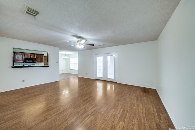 unfurnished living room featuring ceiling fan with notable chandelier, light hardwood / wood-style flooring, french doors, and a textured ceiling