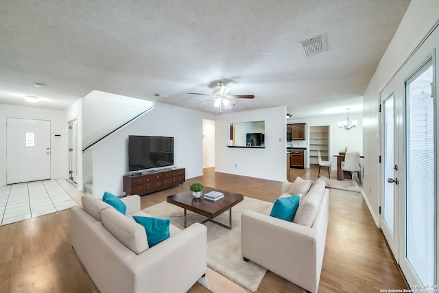 living room featuring ceiling fan with notable chandelier, a textured ceiling, and light wood-type flooring