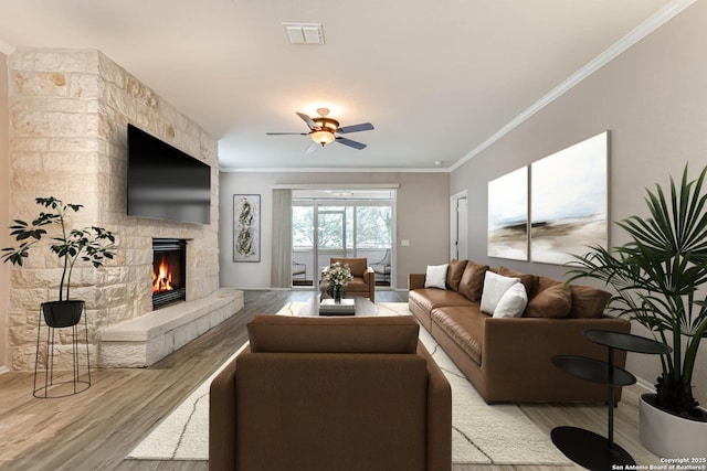 living room with ornamental molding, a stone fireplace, ceiling fan, and light hardwood / wood-style flooring