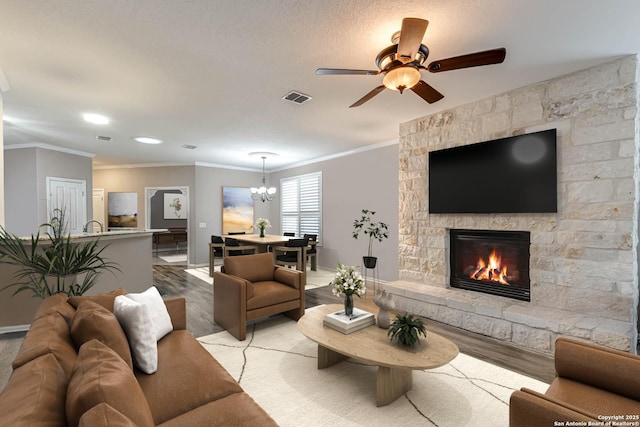 living room with crown molding, a fireplace, ceiling fan with notable chandelier, and light wood-type flooring