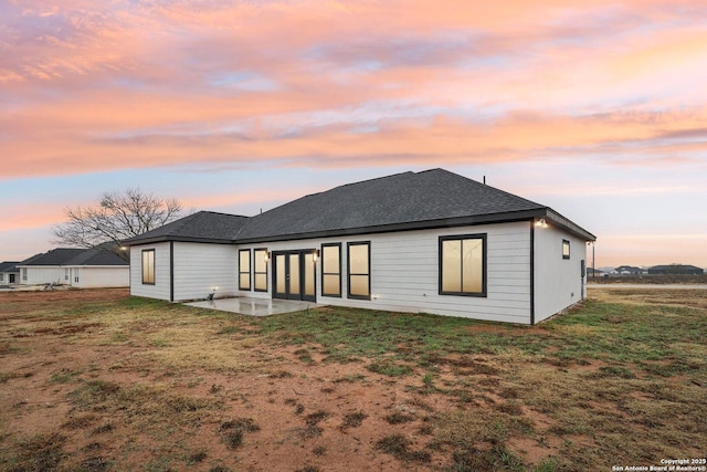 back house at dusk featuring a yard and a patio area