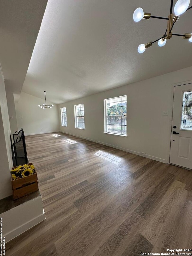 unfurnished living room with wood-type flooring, lofted ceiling, and an inviting chandelier