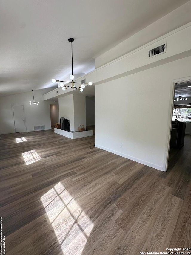 unfurnished living room with an inviting chandelier, vaulted ceiling, and dark hardwood / wood-style floors