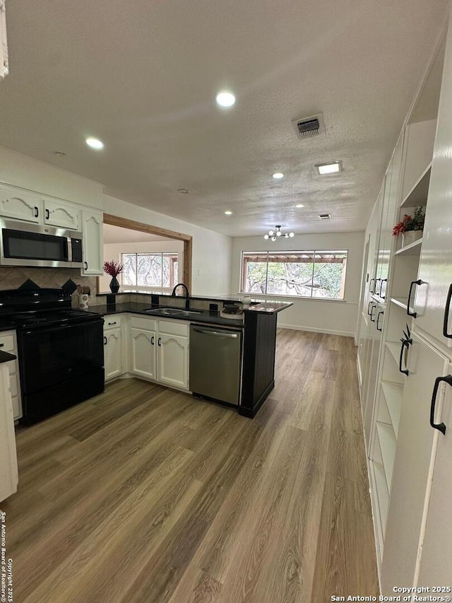 kitchen with sink, hardwood / wood-style flooring, stainless steel appliances, white cabinets, and kitchen peninsula