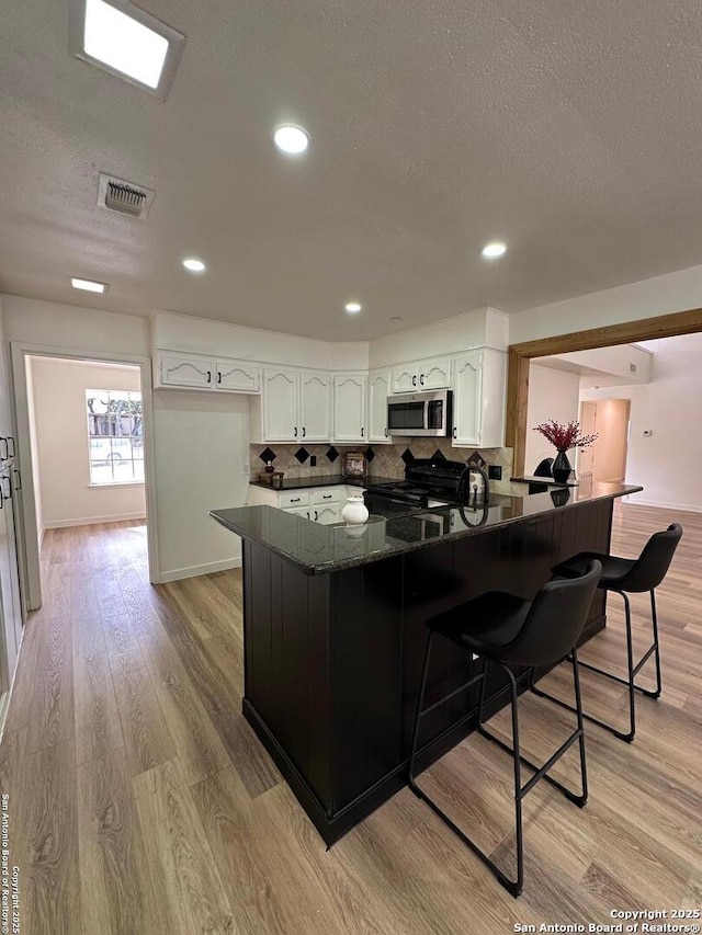 kitchen with white cabinetry, light hardwood / wood-style floors, kitchen peninsula, and a breakfast bar