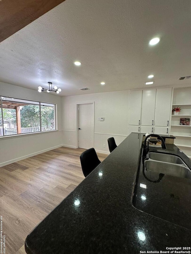 kitchen with sink, light hardwood / wood-style flooring, white cabinetry, dark stone countertops, and a textured ceiling