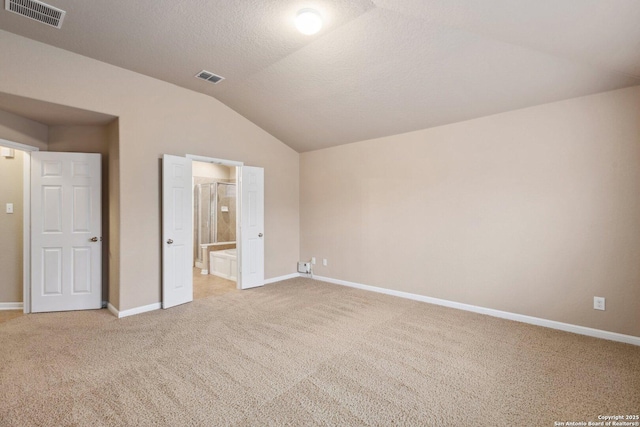 unfurnished bedroom featuring lofted ceiling, carpet floors, connected bathroom, and a textured ceiling