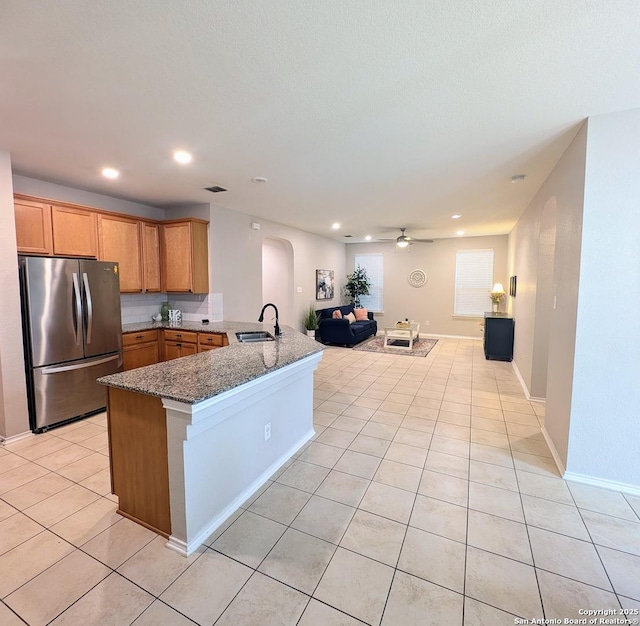 kitchen with sink, light tile patterned floors, stainless steel refrigerator, kitchen peninsula, and dark stone counters