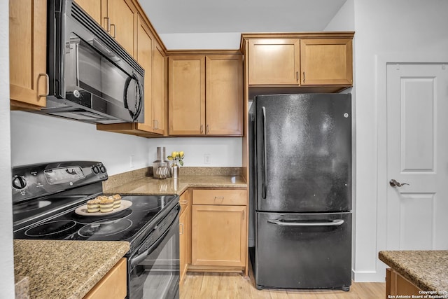 kitchen featuring light stone counters, light hardwood / wood-style floors, and black appliances