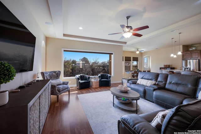 living room featuring a raised ceiling, dark wood-type flooring, sink, and ceiling fan