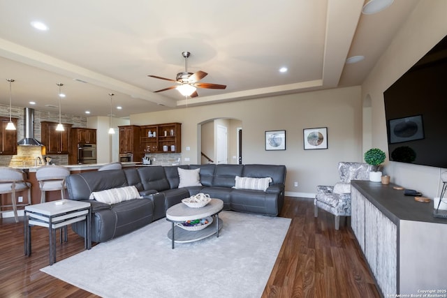 living room with ceiling fan, a tray ceiling, and dark hardwood / wood-style flooring