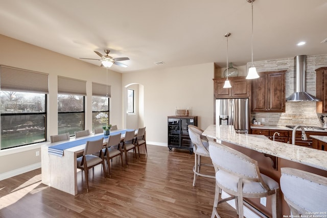 kitchen with hanging light fixtures, light stone counters, tasteful backsplash, stainless steel fridge with ice dispenser, and wall chimney exhaust hood