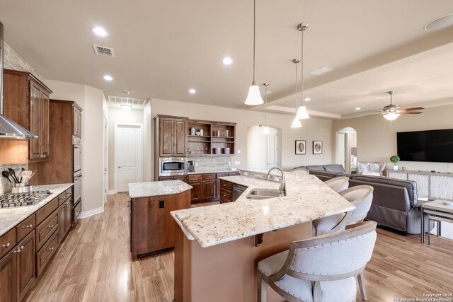 kitchen with sink, light stone counters, appliances with stainless steel finishes, pendant lighting, and a kitchen island with sink