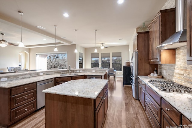 kitchen featuring pendant lighting, wall chimney range hood, sink, stainless steel appliances, and a spacious island