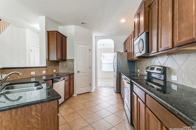 kitchen with light tile patterned flooring, appliances with stainless steel finishes, sink, and dark stone countertops