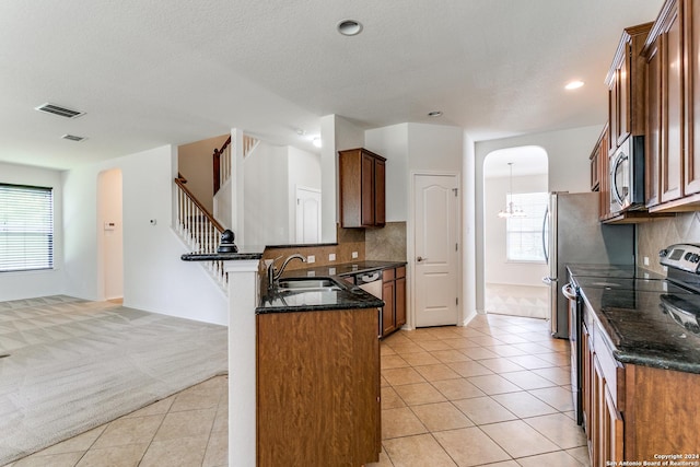 kitchen with light tile patterned flooring, appliances with stainless steel finishes, sink, dark stone counters, and kitchen peninsula