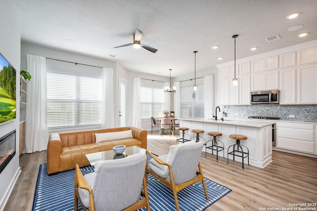 living room with ceiling fan, sink, a textured ceiling, and light wood-type flooring