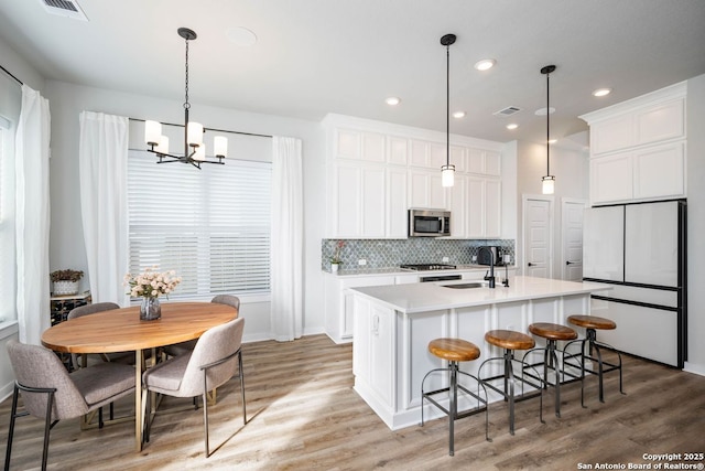 kitchen with sink, decorative light fixtures, white fridge, a kitchen island with sink, and white cabinets