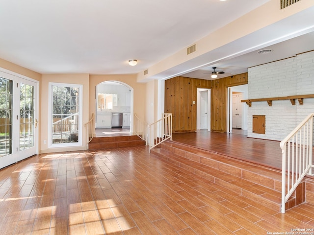 unfurnished living room with hardwood / wood-style flooring, a brick fireplace, ceiling fan, and wood walls