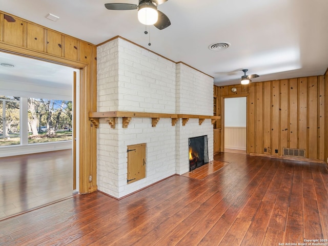 unfurnished living room with dark wood-type flooring, a fireplace, ceiling fan, and wood walls