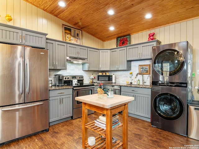 kitchen featuring stainless steel appliances, stacked washer and clothes dryer, dark stone countertops, and wooden ceiling