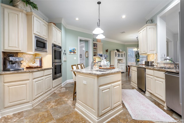 kitchen with stainless steel appliances, cream cabinets, light stone countertops, a kitchen island, and decorative light fixtures