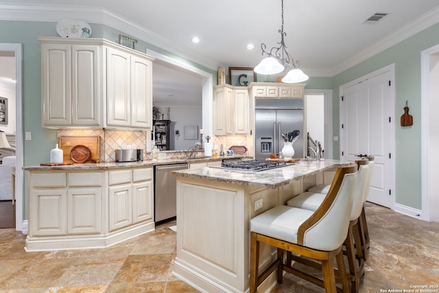 kitchen with appliances with stainless steel finishes, a center island, ornamental molding, light stone countertops, and decorative light fixtures