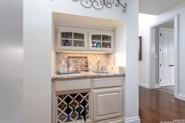 bar with cream cabinets, tasteful backsplash, sink, light stone countertops, and dark wood-type flooring