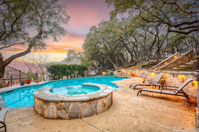 pool at dusk featuring a patio and an in ground hot tub