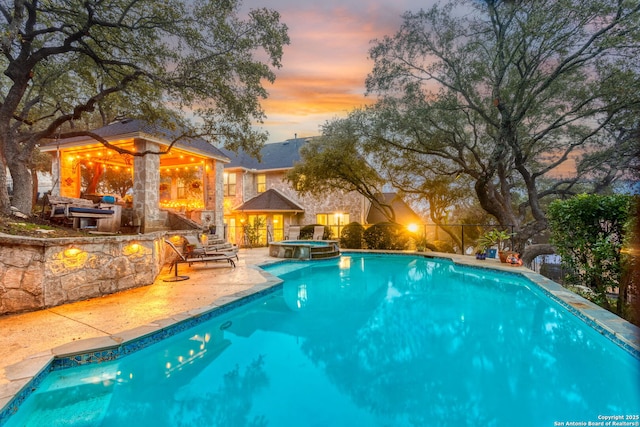 pool at dusk featuring an in ground hot tub and a patio