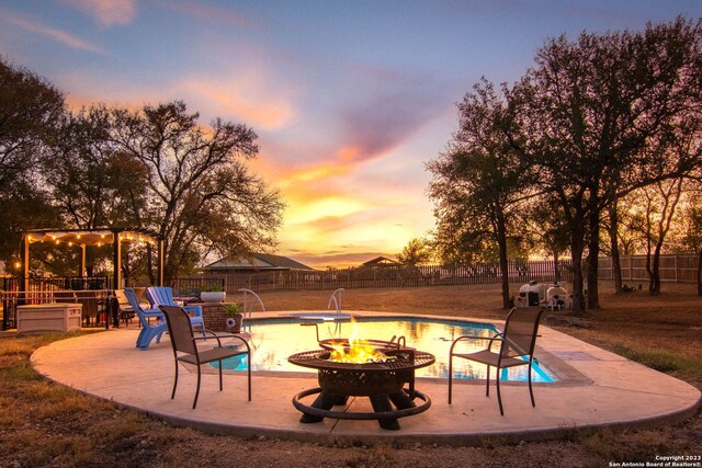 pool at dusk featuring pool water feature and an outdoor fire pit