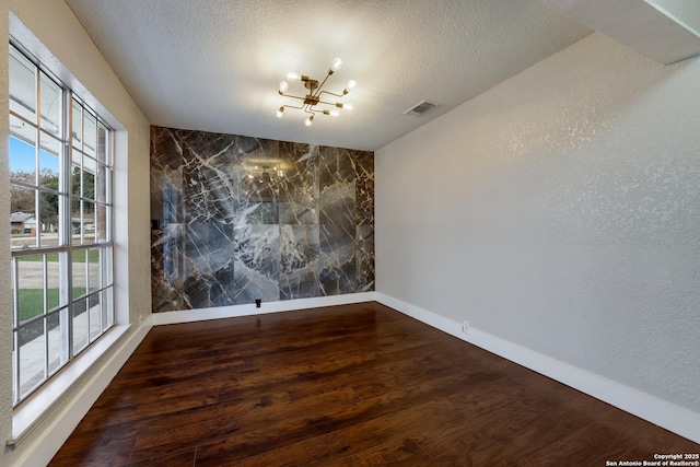 empty room featuring hardwood / wood-style floors, a chandelier, and a textured ceiling