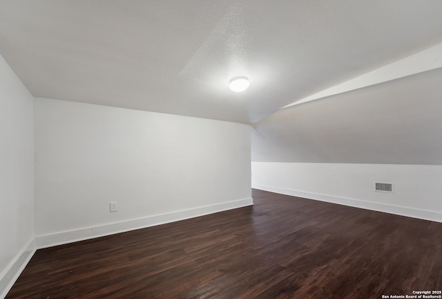 bonus room with lofted ceiling, dark wood-type flooring, and a textured ceiling